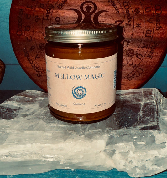 Candle jar labeled 'Mellow Magic' from Sacred Wild Candle Company on a crystal surface with a wooden board in the background.