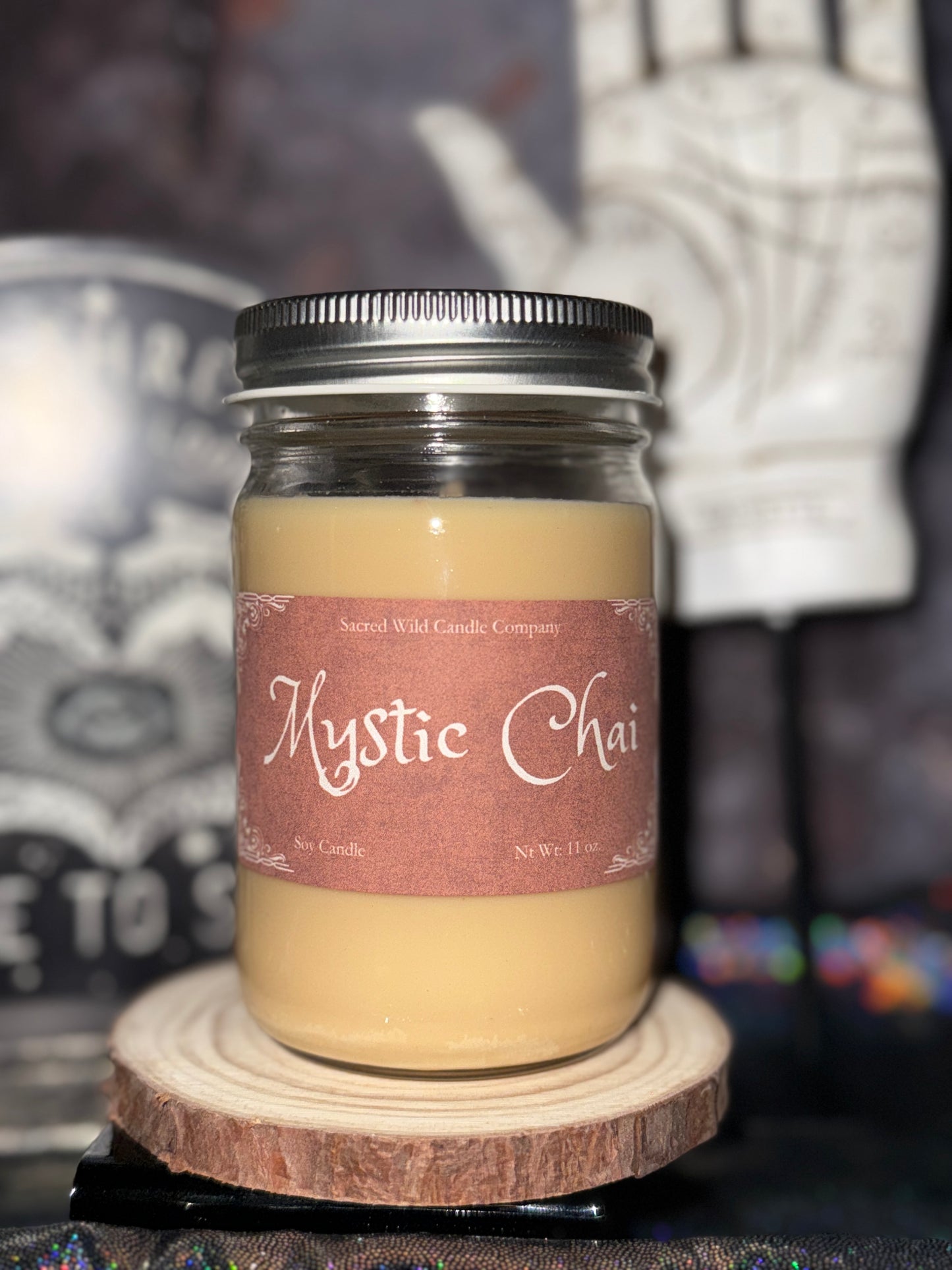 Candle jar labeled 'Mystic Chai' on a wooden coaster with a blurred background