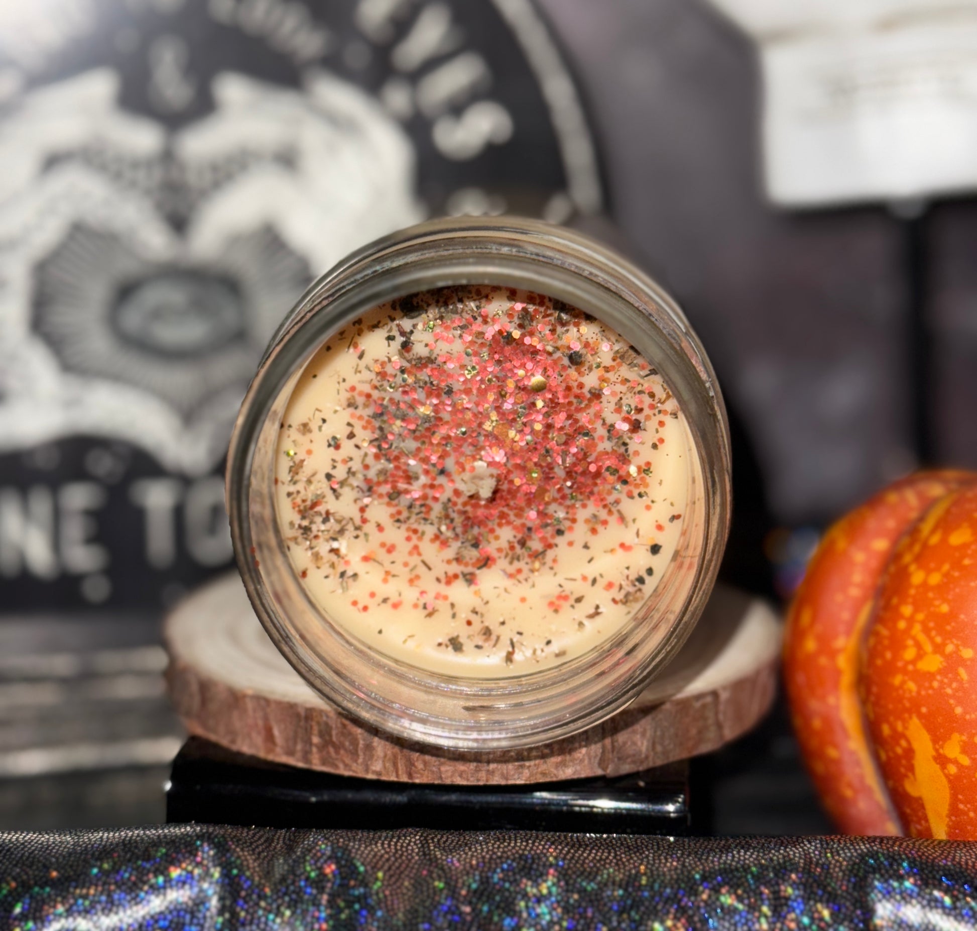 Crones Cottage candle with colorful specks on a wooden stand with a blurred background