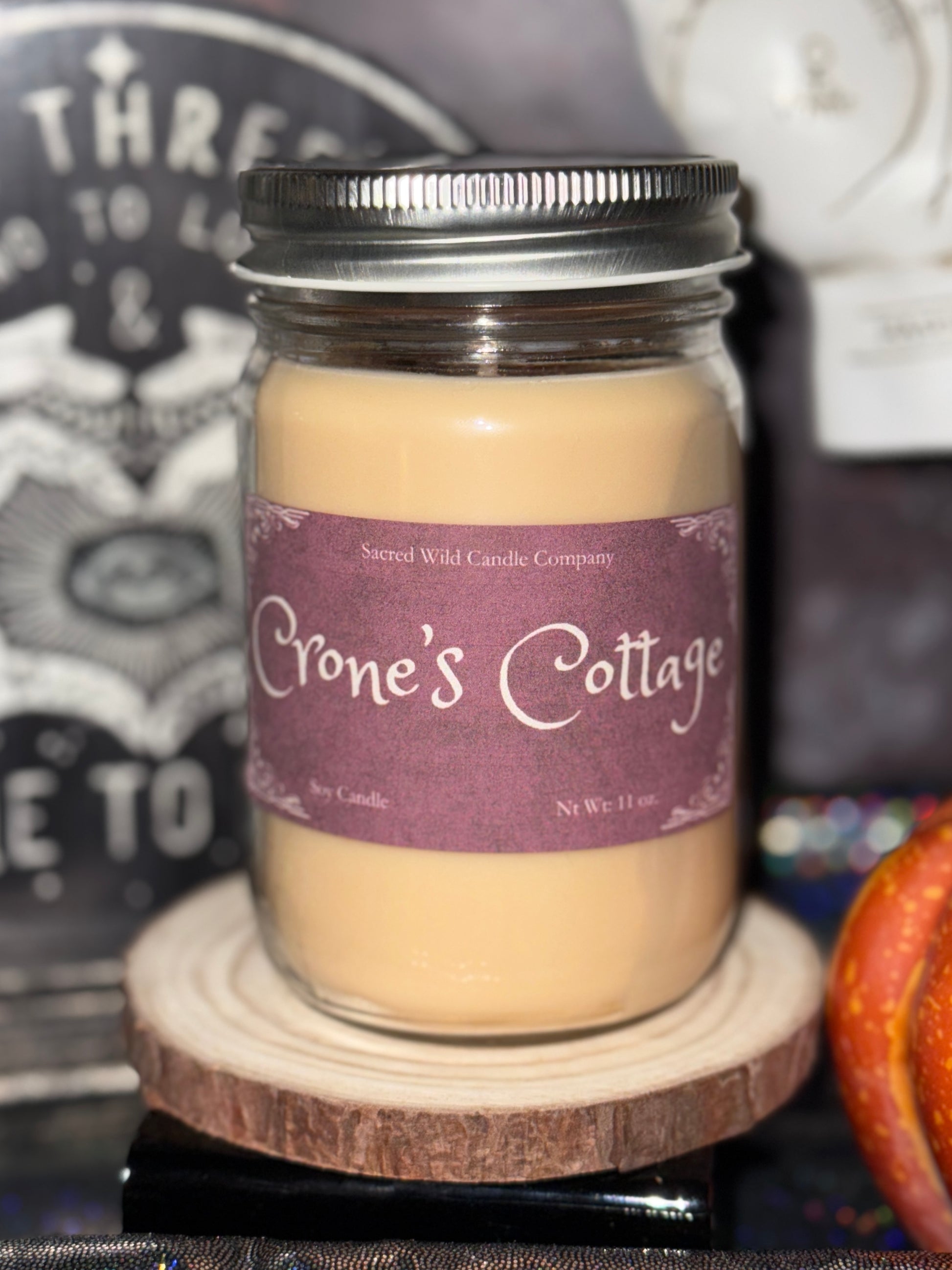 Jar of candle labeled 'Crone's Cottage' on a wooden coaster with a blurred background.
