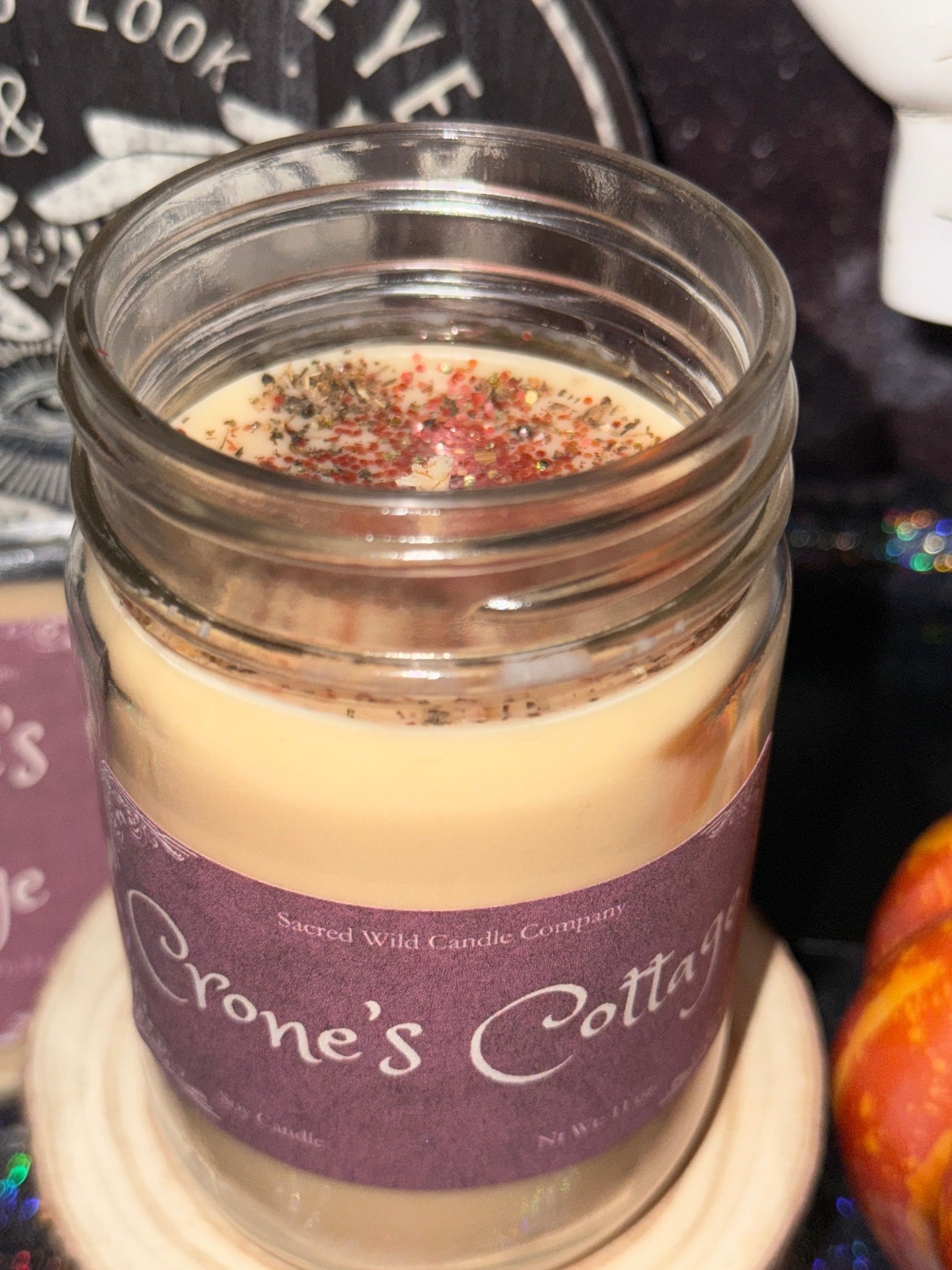 Jar of Crone's Cottles candle with a purple label on a dark background